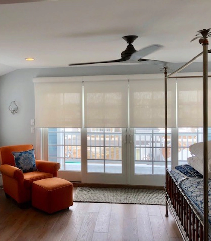 Bedroom with white roller shades on a large window and sliding door, soft filtered daylight