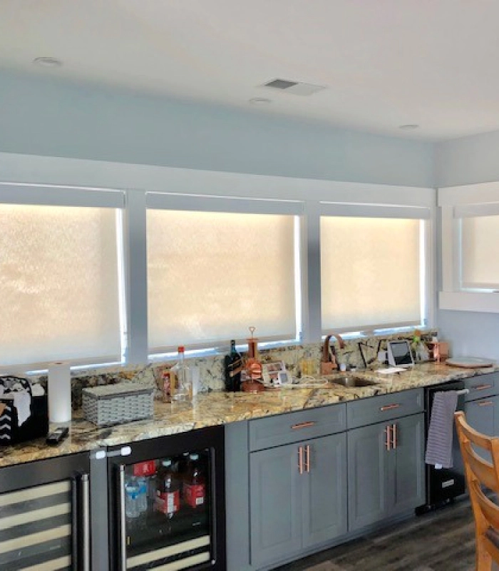 Modern kitchen with three large windows fitted with light roller shades and granite countertops